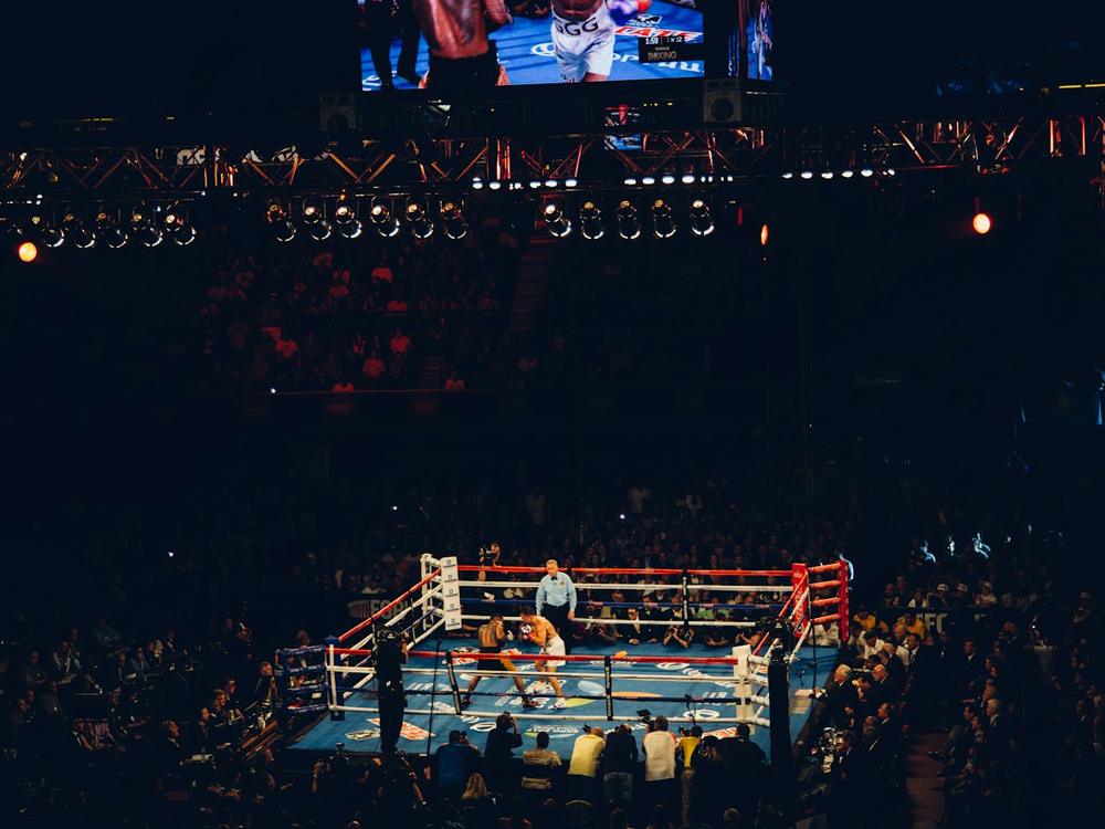 A packed arena watching a bout under the ring lights